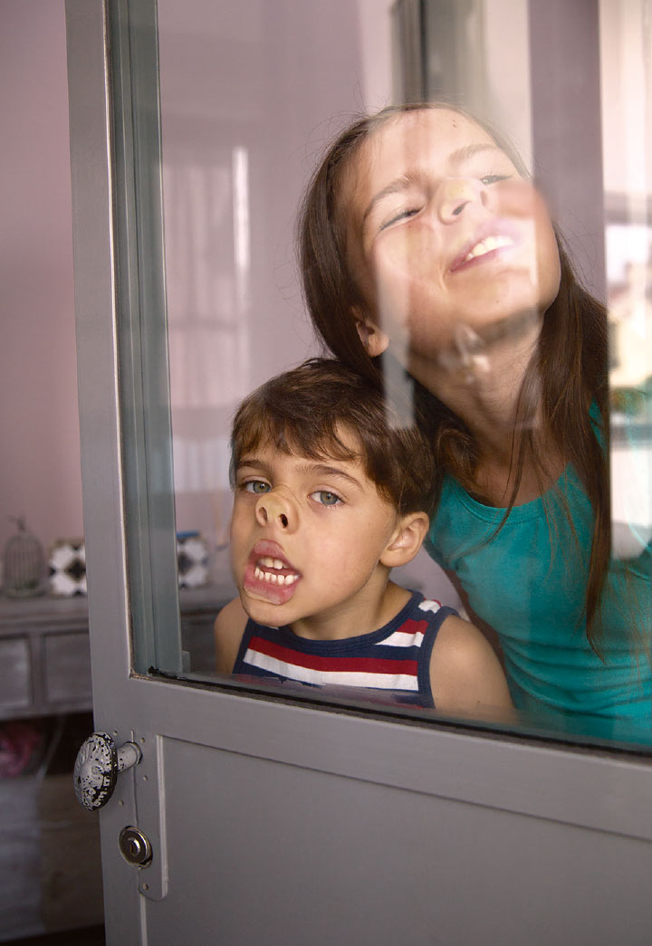 Photographie lifestyle de familles et d'enfants qui font des grimaces devant une vitre de maison
