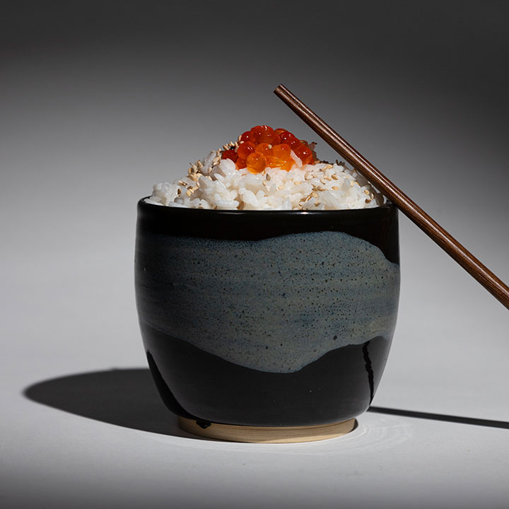 Photographie d'un bol de riz épicé et des baguettes en bois sur fond noir